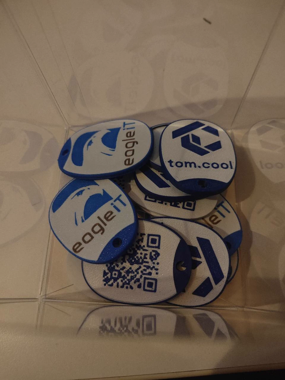 Blauw-witte sleutelhangers met logo en QR-code in een bewaarbakje
